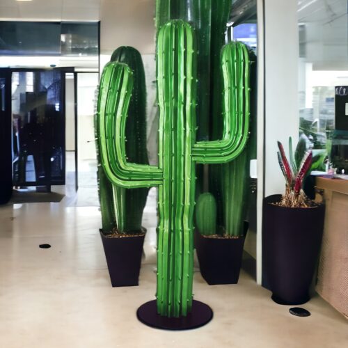 Large green cactus sculpture placed indoors with other potted cacti.
