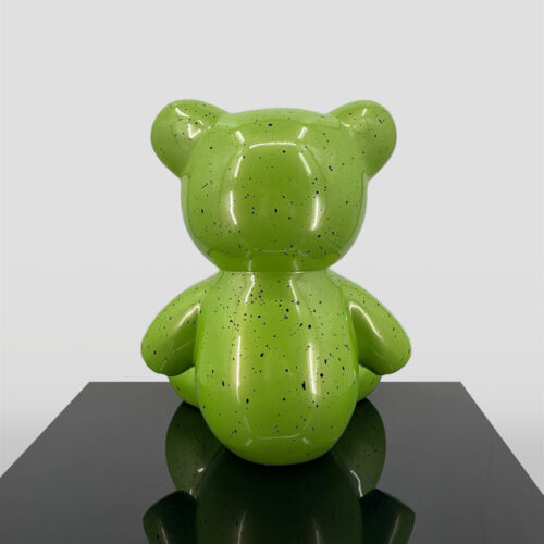 Green speckled teddy bear sculpture on a black reflective surface.