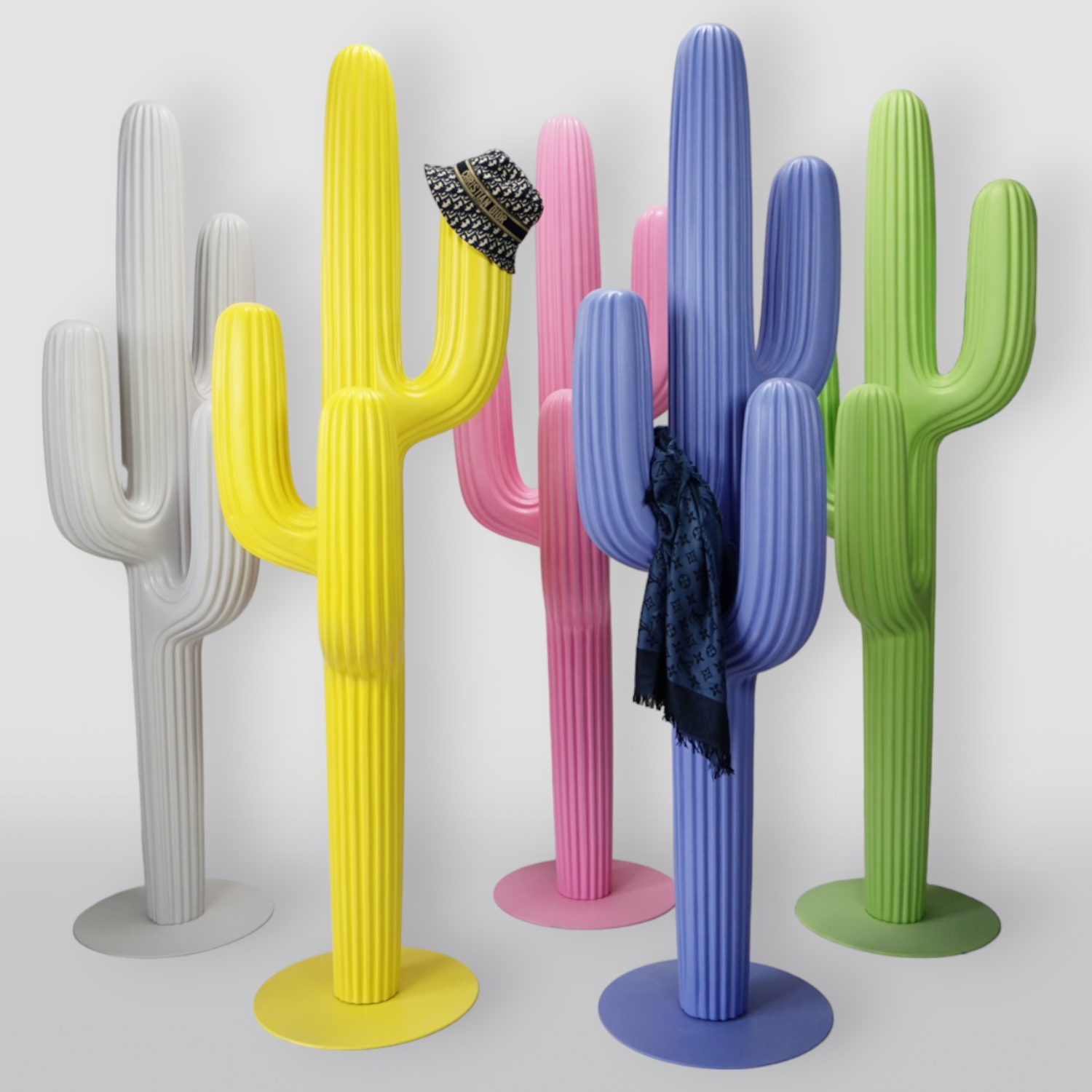 Pastel Yellow Hanger - Cactus 3 Group of colorful cactus-shaped coat racks, each in a different bright color (gray, yellow, pink, blue, and green), with a hat and a scarf hanging on them.