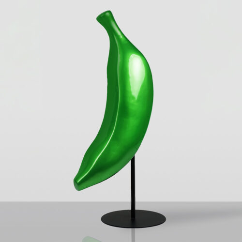 Glossy green banana-shaped sculpture mounted on a slim black metal stand with a round base, placed on a reflective surface against a plain light gray background.