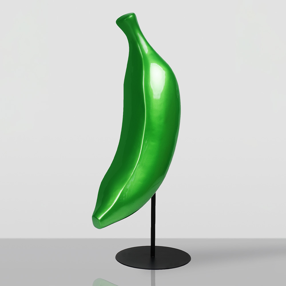 Chrome Banana 1 Glossy green banana-shaped sculpture mounted on a black metal stand with a round base on a gray reflective surface against a light gray background.