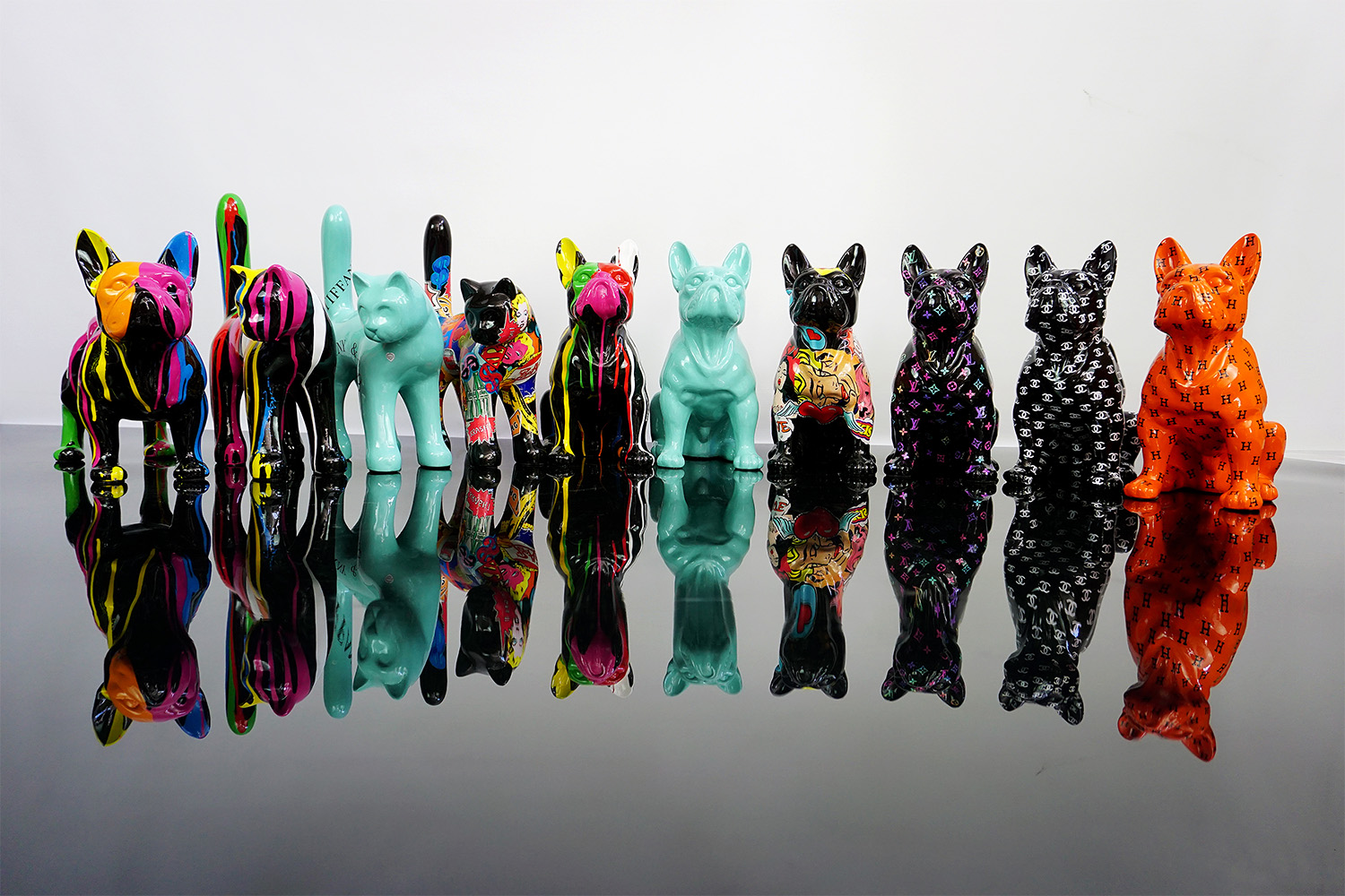 Colorful sculptures of cats and dogs in various artistic designs lined up on a reflective surface.