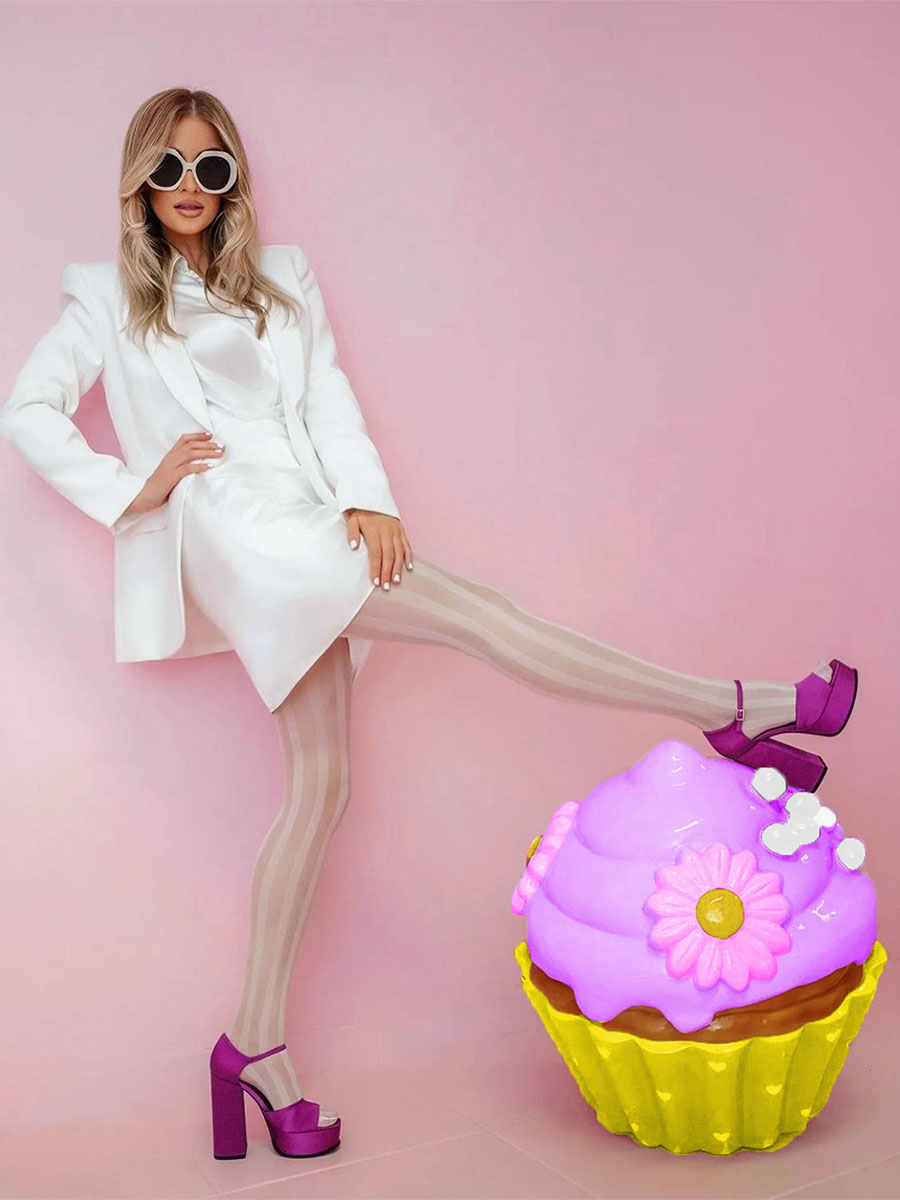 Colorful Cupcake for Sweet Home Bakery in Lagos, Portugal 4 Kobieta w białym stroju, okularach przeciwsłonecznych i fioletowych butach na wysokim obcasie na tle różowej ściany, z fioletowo-żółtą dekoracyjną babeczką.