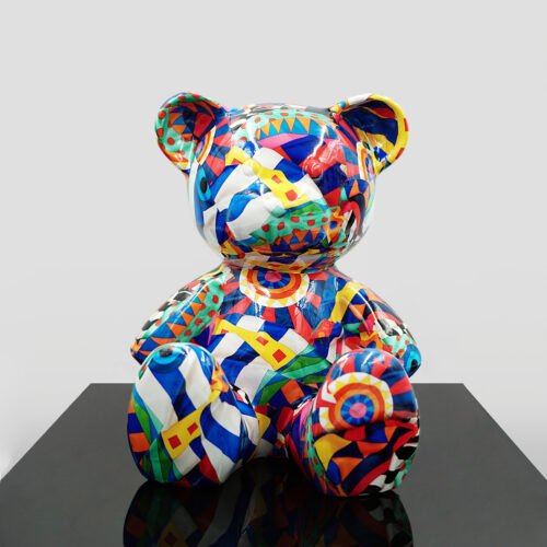 Colorful teddy bear sculpture with geometric and abstract patterns, displayed on a black surface against a plain gray background.