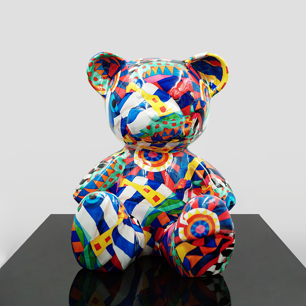 Small Sitting Bear - Mosaic 1 Colorful teddy bear sculpture with geometric and abstract patterns, displayed on a black surface against a plain gray background.