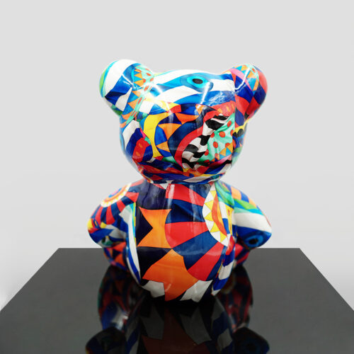 A colorful geometric patterned bear sculpture displayed on a black reflective surface against a plain background.