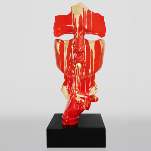 Modern sculpture of a red and yellow face with a hand in a shushing gesture on a black base.