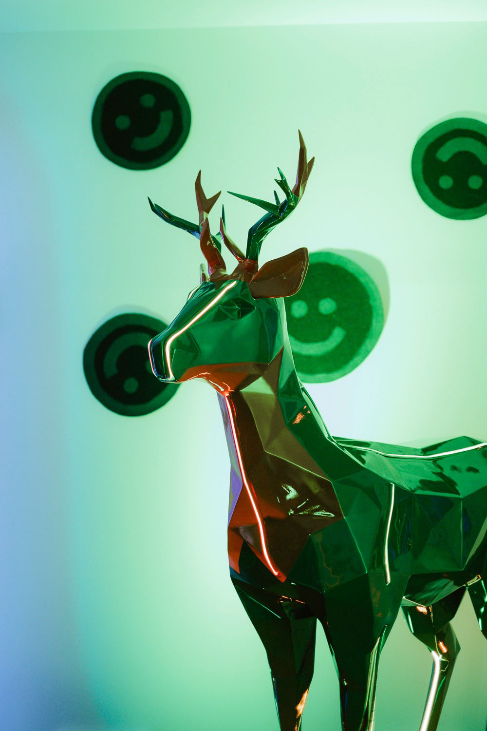 Jägermeister Deer with Lighting 7 Metaliczna rzeźba renifera na tle świecących, zielonych emoji.
