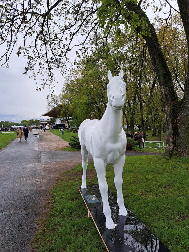 Biała rzeźba konia stojąca na trawniku w parku.