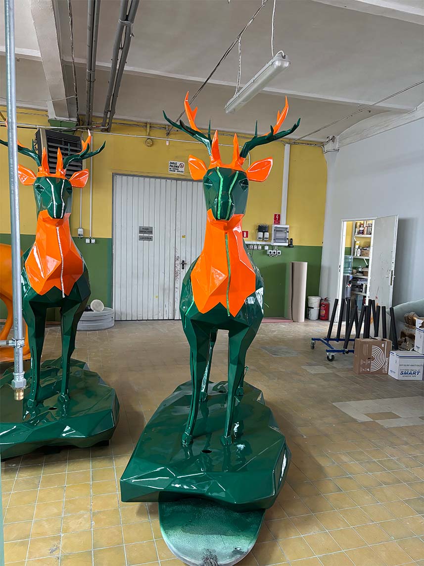Jägermeister Deer with Lighting 6 Rzeźby jeleni wykonane z pomarańczowego i zielonego metalu w warsztacie.