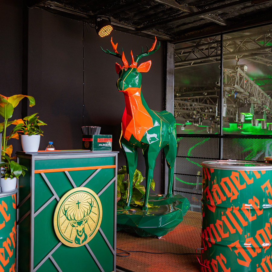 Colorful geometric deer sculpture in a themed bar setup featuring Jägermeister branding and green-orange decor.