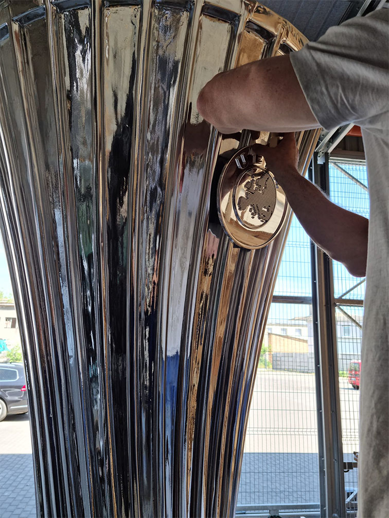 Ręce osoby montującej lub naprawiającej dużą, błyszczącą metalową tubę muzyczną w zadaszonym, przemysłowym otoczeniu