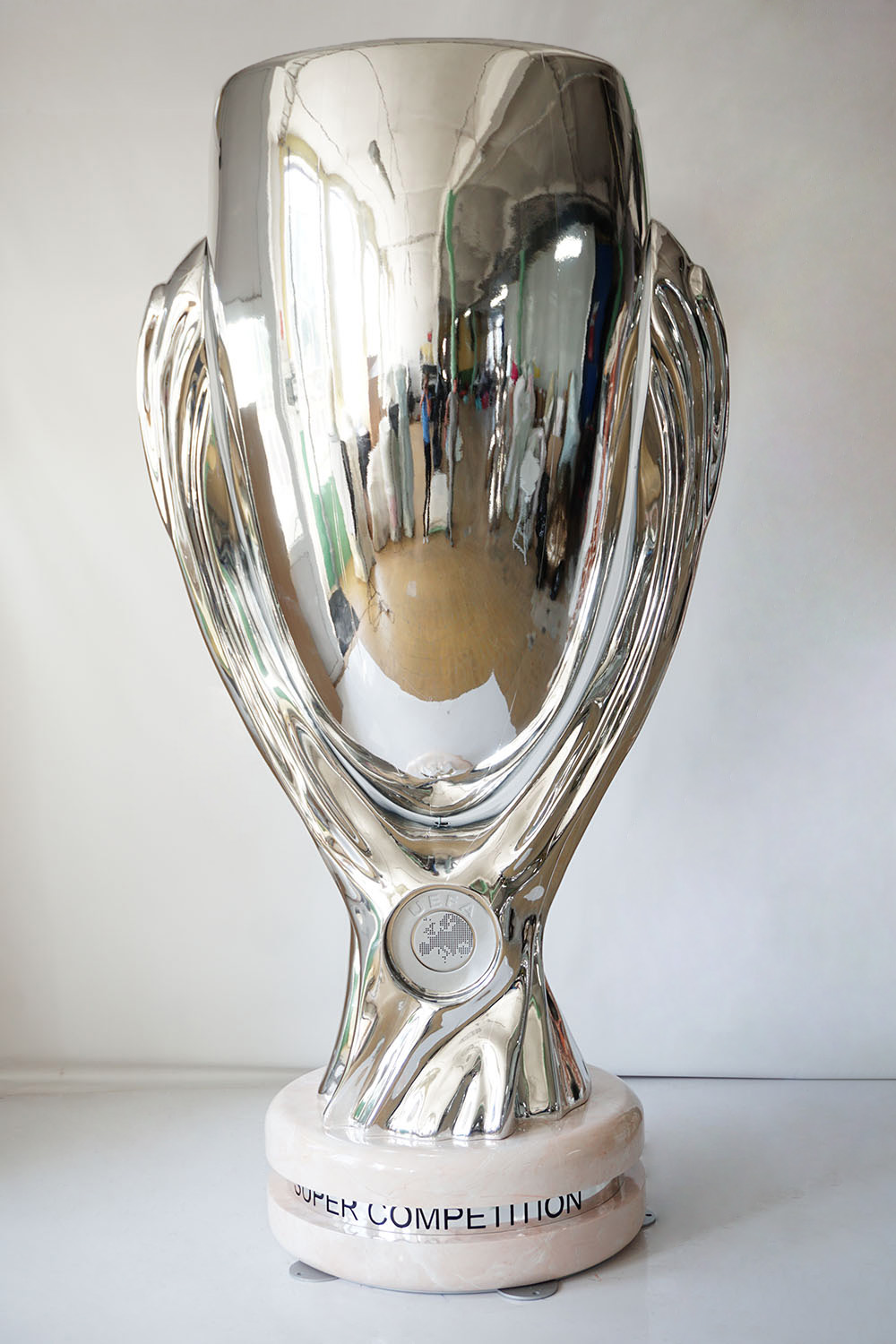 Large UEFA Super Cup Figure for the 2024 Championship 4 srebrny puchar UEFA Super Cup na marmurowej podstawie stojący na białym tle, odbijający otoczenie w błyszczącej powierzchni
