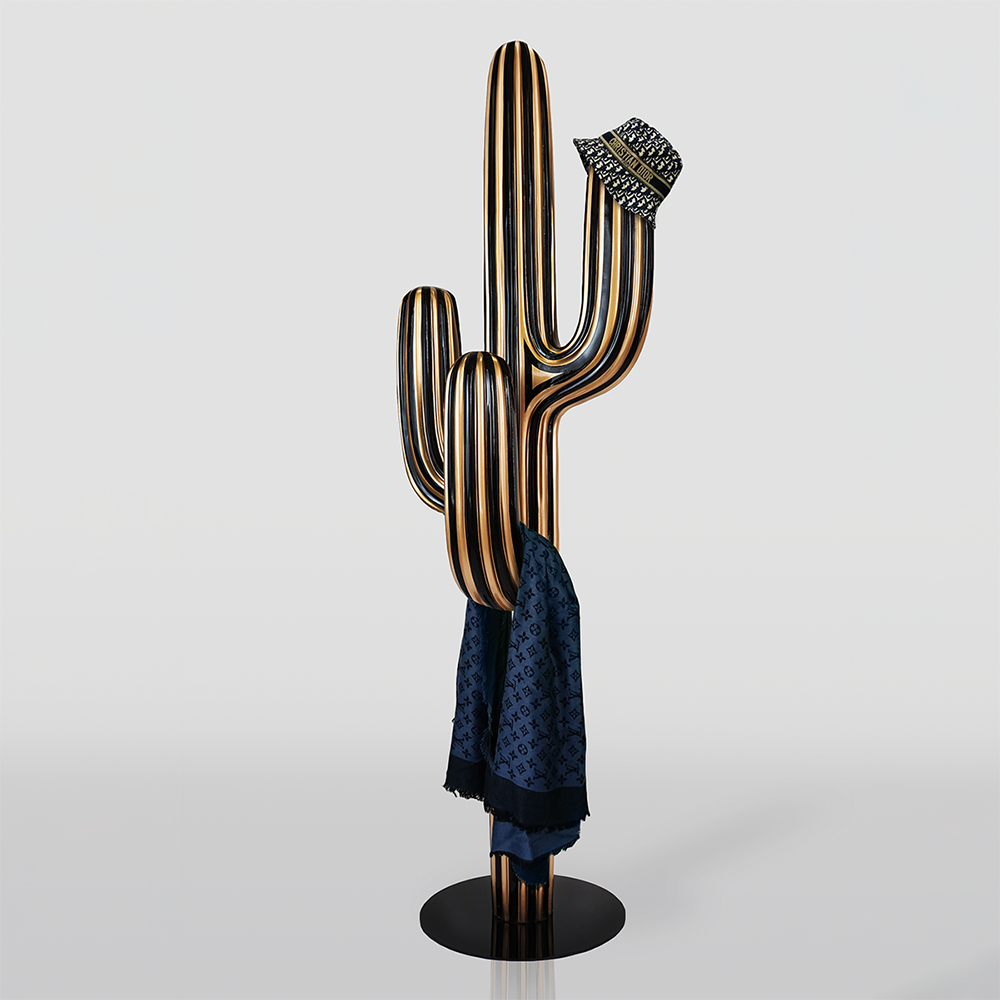 Cactus Hanger Gold-Black 2 Metal sculpture of a striped cactus with a luxury patterned bucket hat on one arm and a blue designer scarf hanging on another arm against a plain light background.