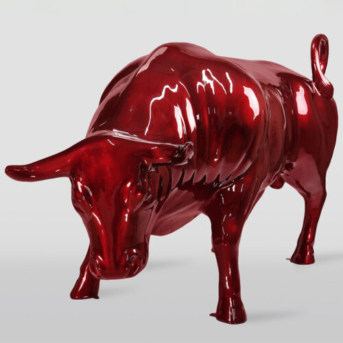 Glossy red sculpture of a bull with head lowered and tail curled, standing on a plain light gray background