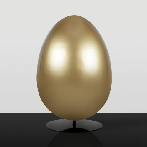 Large smooth golden egg sculpture displayed on a black reflective surface against a light gray background