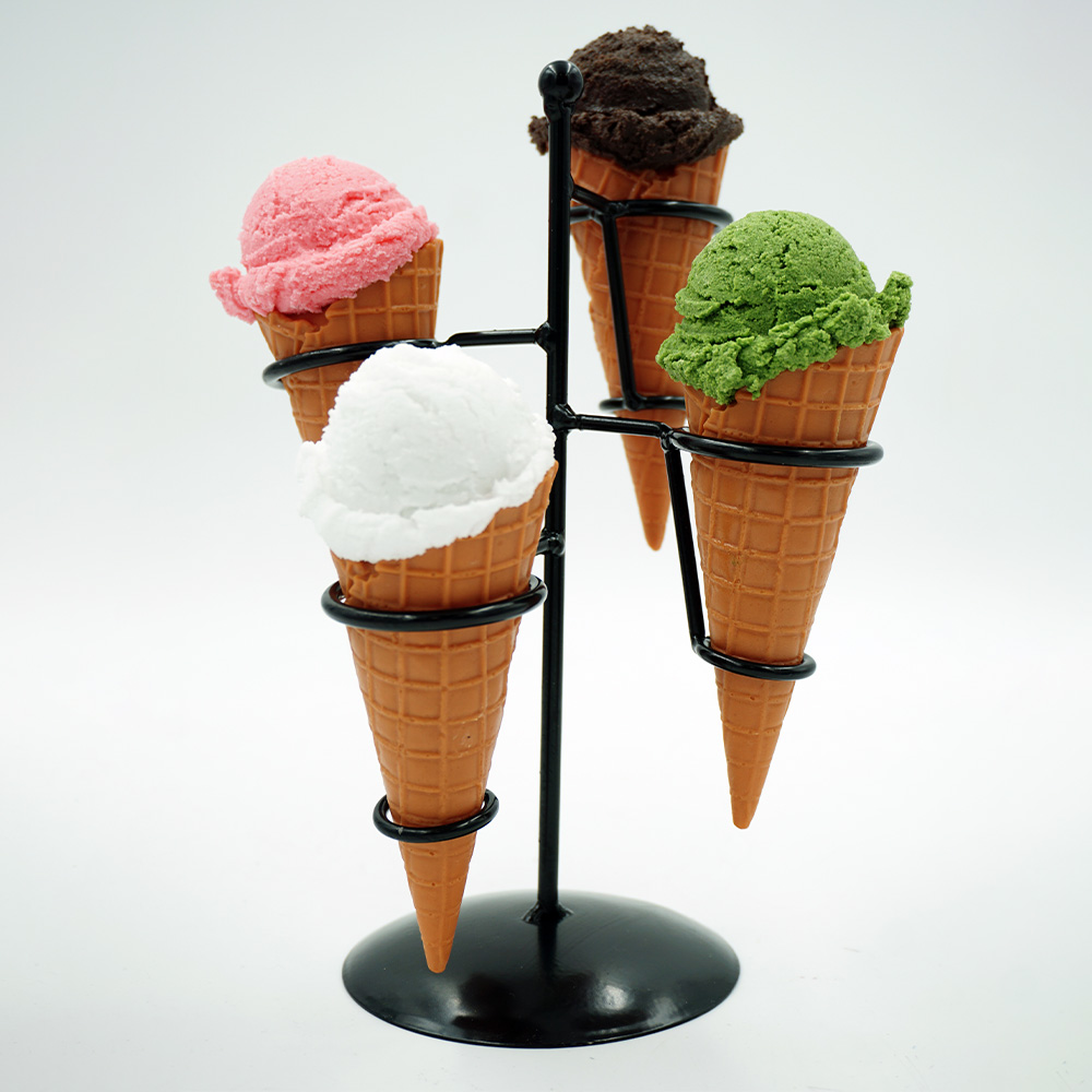 Decorative Ice Cream Basket – Motif III 3 Four ice cream cones with scoops in pink, white, dark brown, and green colors placed in a black metal ice cream cone holder against a white background.