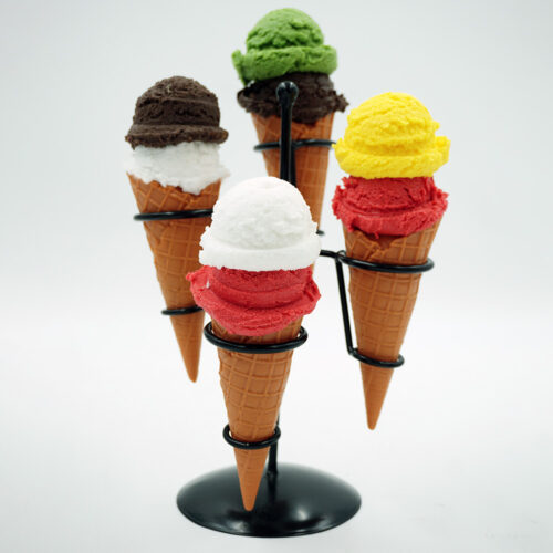 Five ice cream cones in a black metal stand, each cone topped with two scoops of different colored ice cream including green, brown, white, red, and yellow against a plain white background.