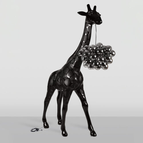 Black glossy giraffe sculpture with a cluster of shiny black spherical shapes hanging from its mouth by a thin string, set against a plain light gray background.