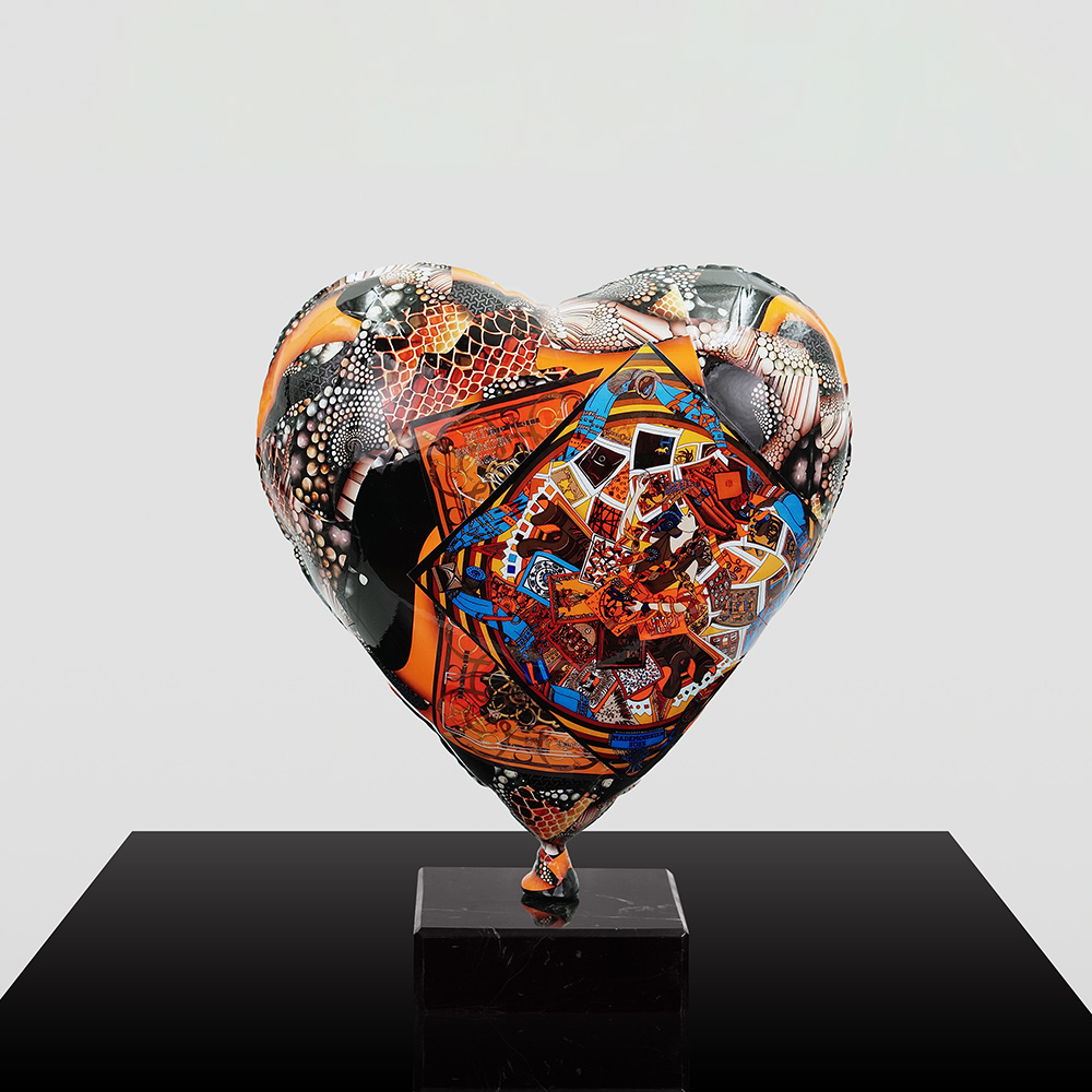Decorative Heart-Shaped Balloon Figurine 9 Heart-shaped sculpture with a complex mixed pattern of orange, blue, black, and white, displayed on a black marble pedestal against a light gray background.