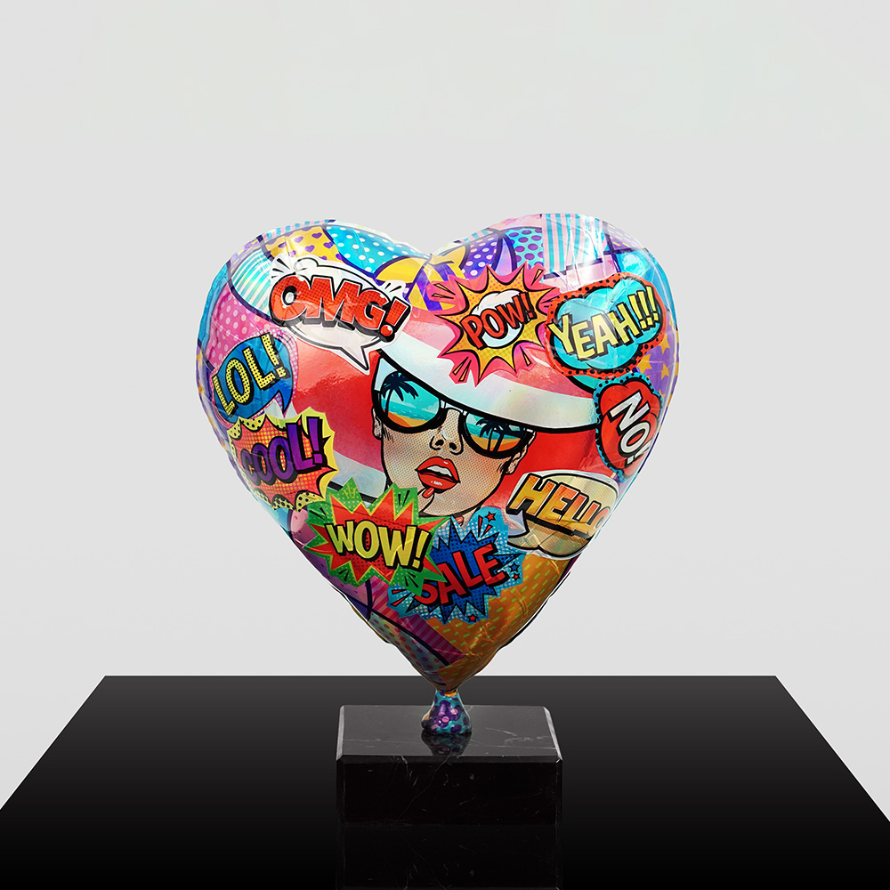 Decorative Heart-Shaped Balloon Figurine 15 Colorful heart-shaped balloon with pop art style graphics including a woman wearing sunglasses and words like OMG, POW, YEAH, LOL, COOL, WOW, SALE, HELLO, and NO, mounted on a black pedestal against a light gray background.