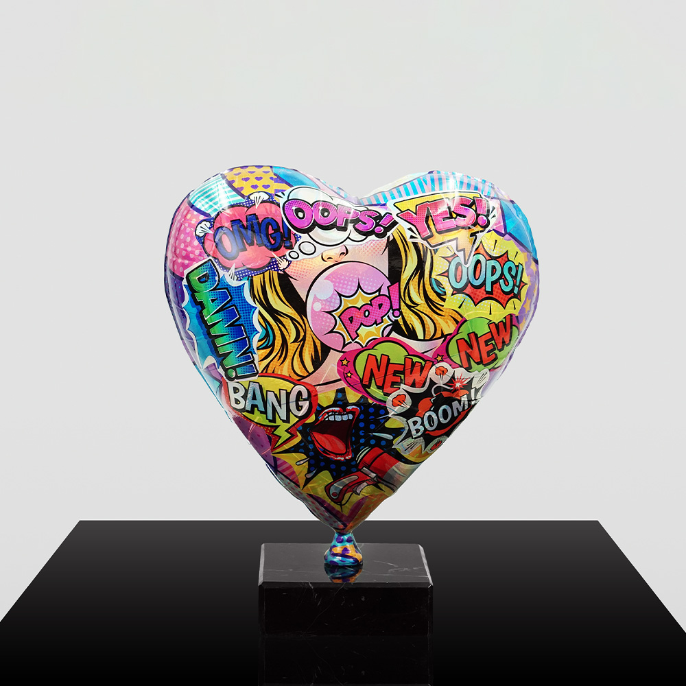 Decorative Heart-Shaped Balloon Figurine 4 Heart-shaped sculpture with a colorful comic-style design featuring words like OMG, Oops, Yes, Bang, New, Pop, and Boom, mounted on a black rectangular base against a plain light background.
