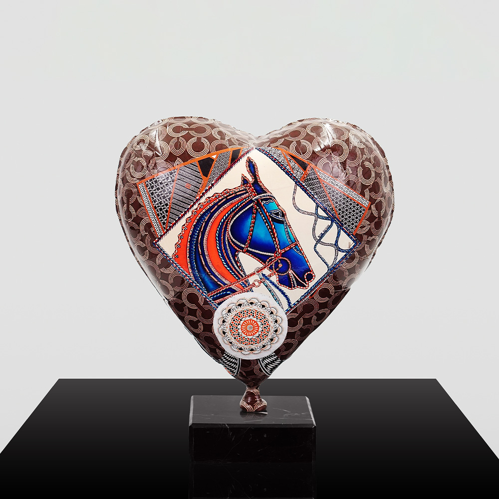 Decorative Heart-Shaped Balloon Figurine 12 Heart-shaped balloon with a pattern of intertwined circles and a central design featuring a blue and red stylized horse head, resting on a black pedestal against a plain light background