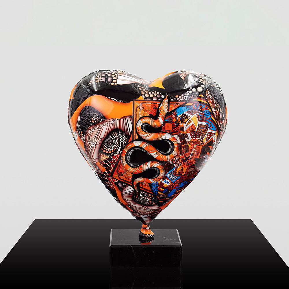 Decorative Heart-Shaped Balloon Figurine 2 Heart-shaped sculpture with intricate patterns in black, orange, white, and blue, featuring snake and abstract designs, mounted on a black square base against a plain gray background.