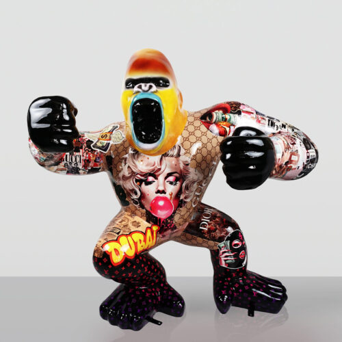 Colorful gorilla sculpture with black fists and feet, a yellow and blue open-mouthed face, decorated with pop art images including a woman blowing bubblegum, brand logos like Gucci, Dior, Chanel, Louis Vuitton patterns, and the word 'Dubai' in yellow and red on one leg.