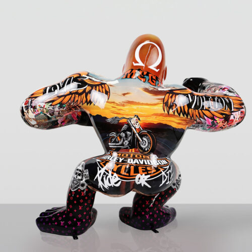 Decorative crouching gorilla statue covered in Harley-Davidson and various graffiti-style artwork, featuring a sunset with mountains, motorcycle image, and wings, with black and red patterned legs, set against a plain light gray background.