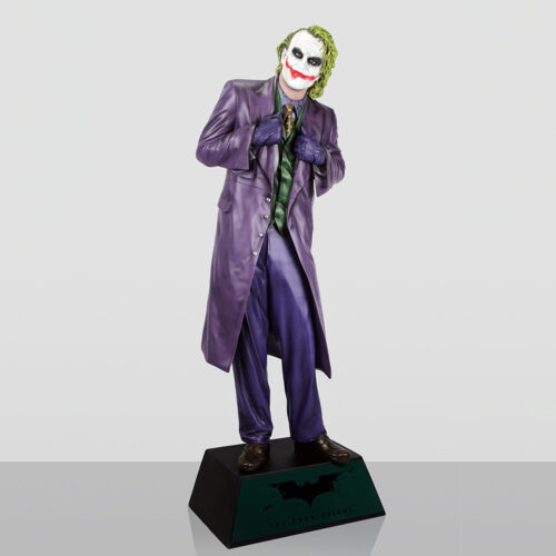 Figurine of the Joker character from The Dark Knight movie, dressed in a purple suit with a green vest and tie, standing on a black base with the Batman logo and text 