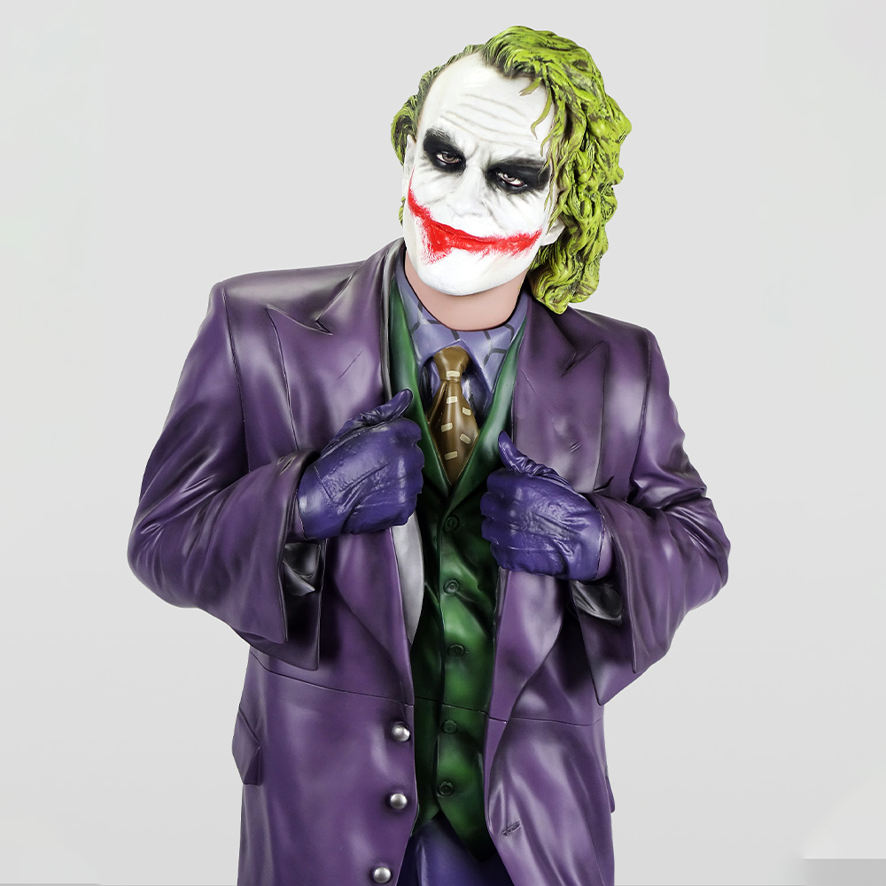 Decorative Figure – Joker 2 Person dressed as the Joker character, wearing a purple suit jacket, green vest, brown tie, purple gloves, with white face paint, black eye makeup, red painted smile, and green hair, posing against a plain light background.