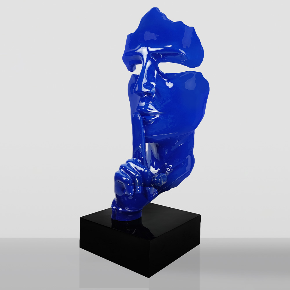 Large Mask on Stand – Blue 2 Glossy blue sculpture of a fragmented human face with a finger held up to the lips in a shushing gesture, mounted on a black rectangular base against a light gray background.