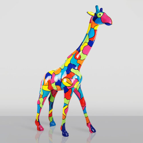 Colorful giraffe sculpture covered in irregular, multicolored patches standing on a reflective surface against a plain light grey background